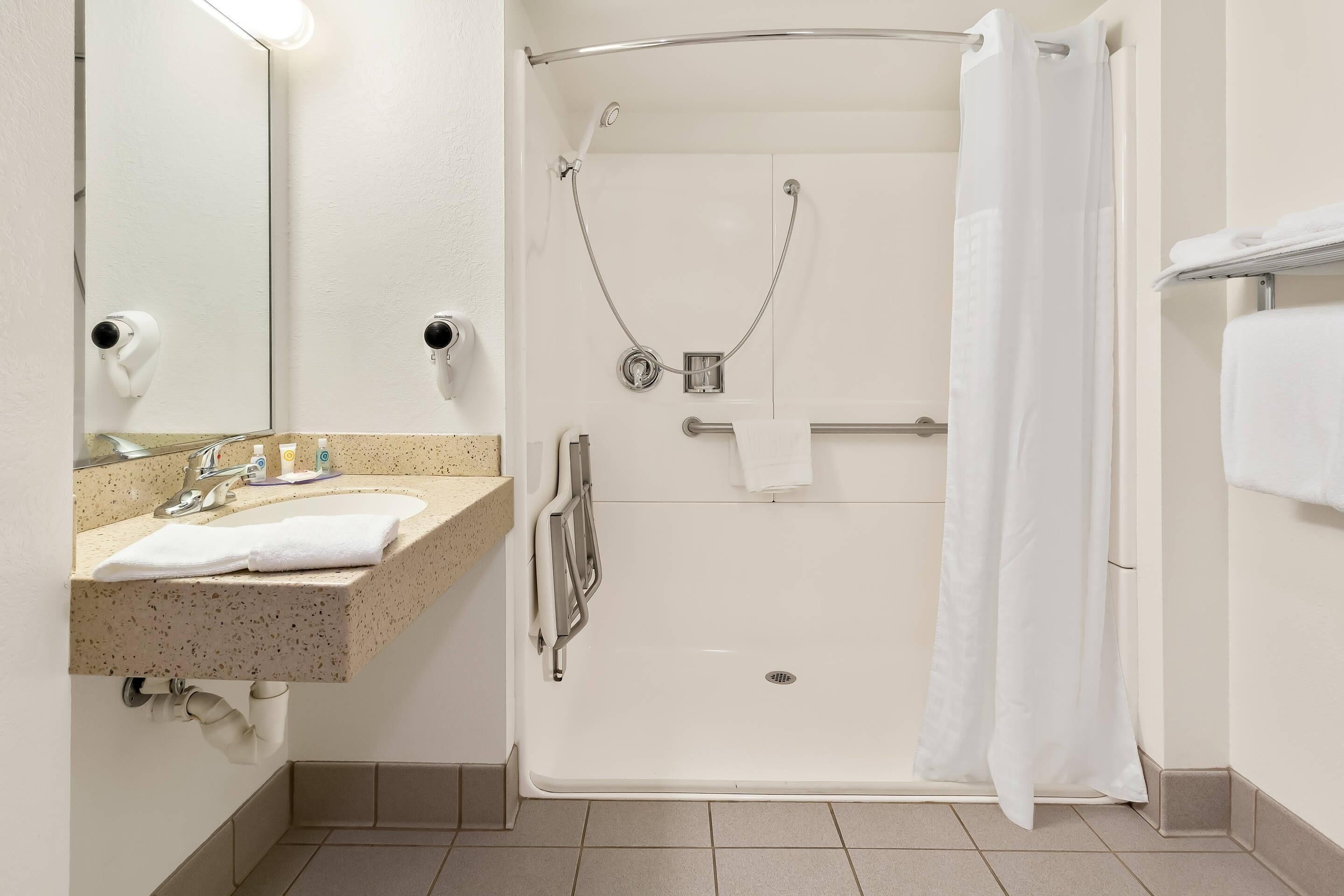 A bathroom with a sink, mirror, shower, and towel rack.