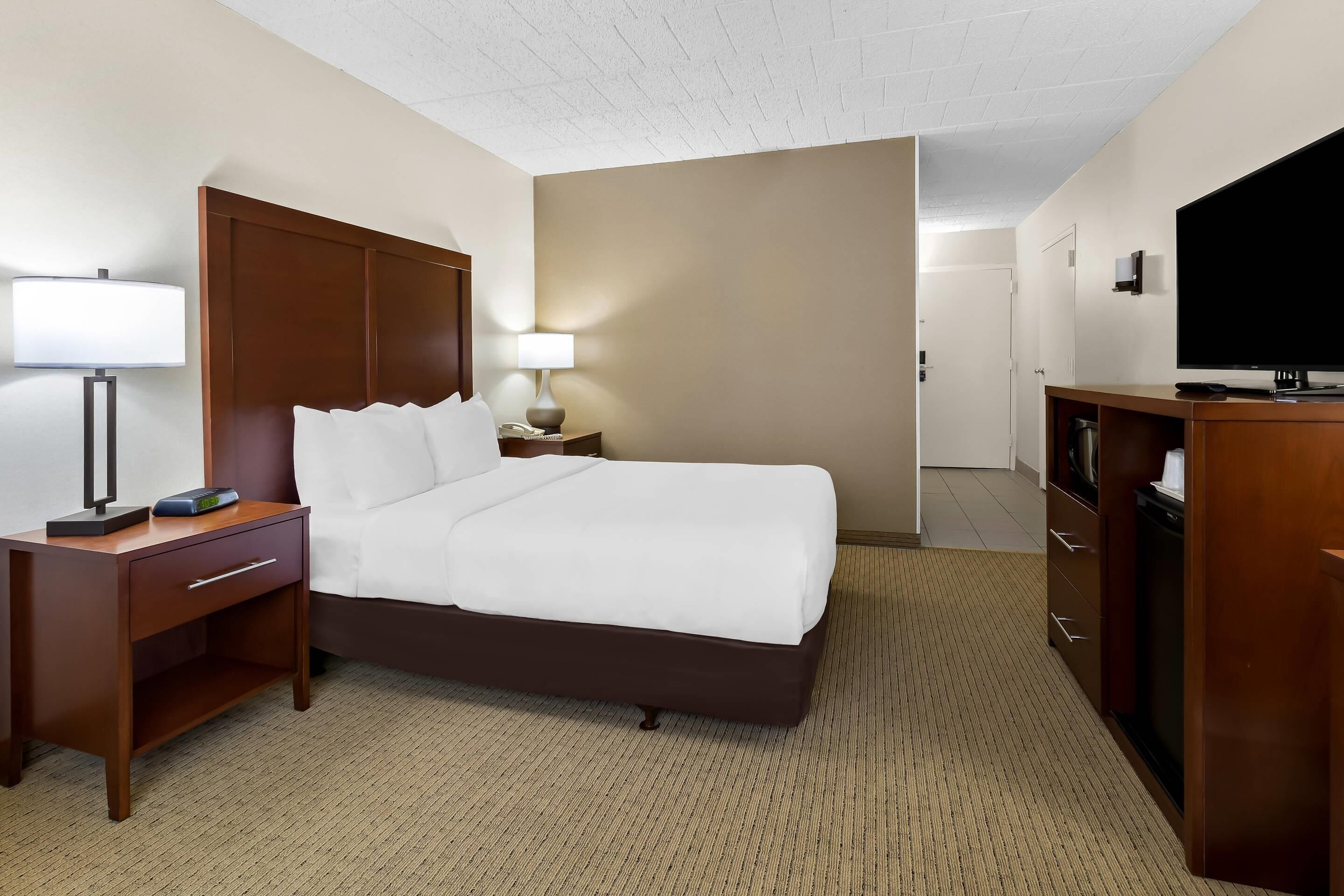 Une chambre d’hôtel comprenant un lit, une table de chevet avec une lampe, une télévision et une commode.