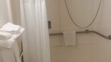 A shower area with a white curtain, a towel rack, and a handheld showerhead.