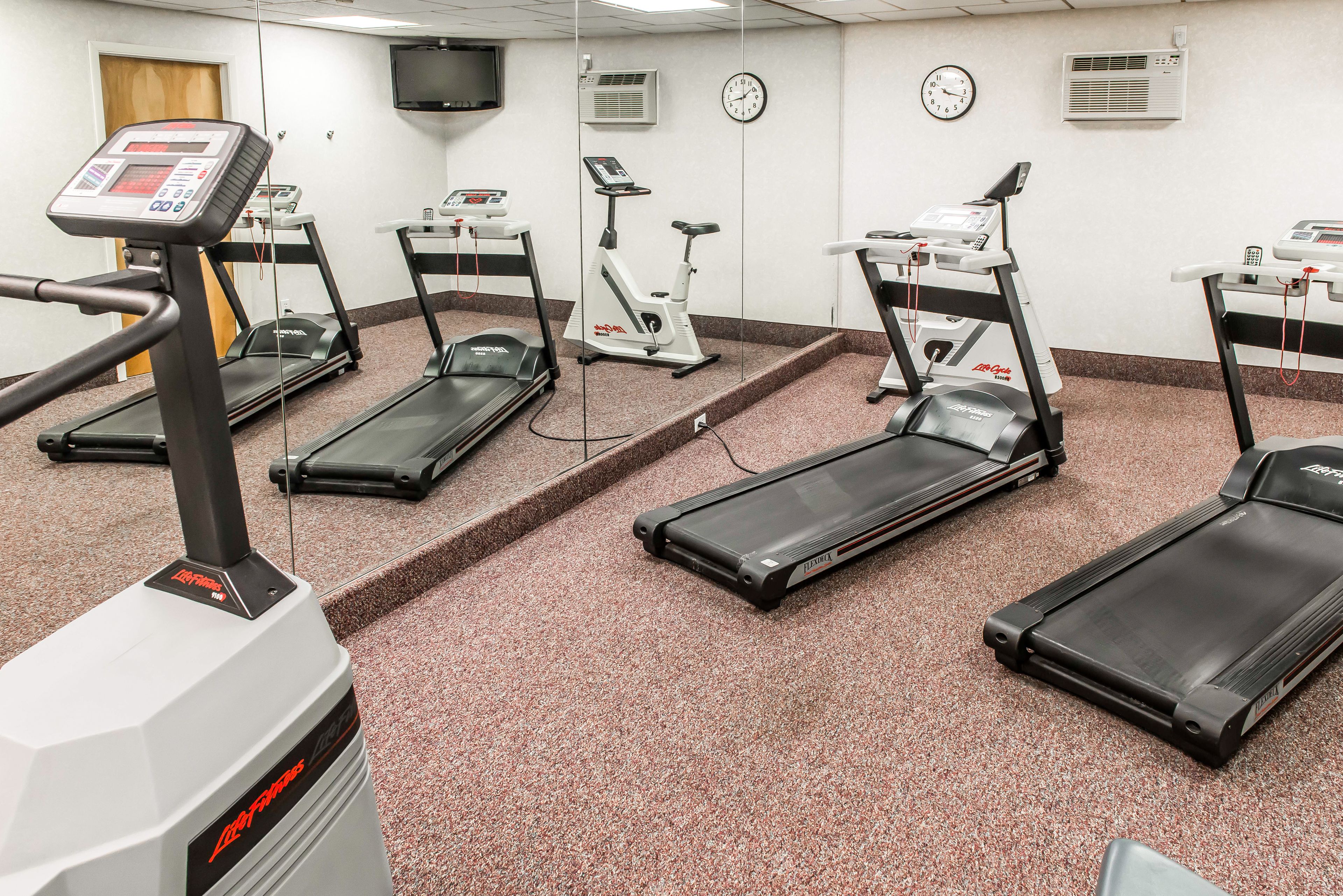 A fitness room with treadmills, an elliptical, and a stationary bike, equipped with various fitness machines and a digital display.