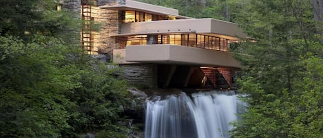 Una casa moderna construida sobre un cascada, rodeada de un bosque denso.