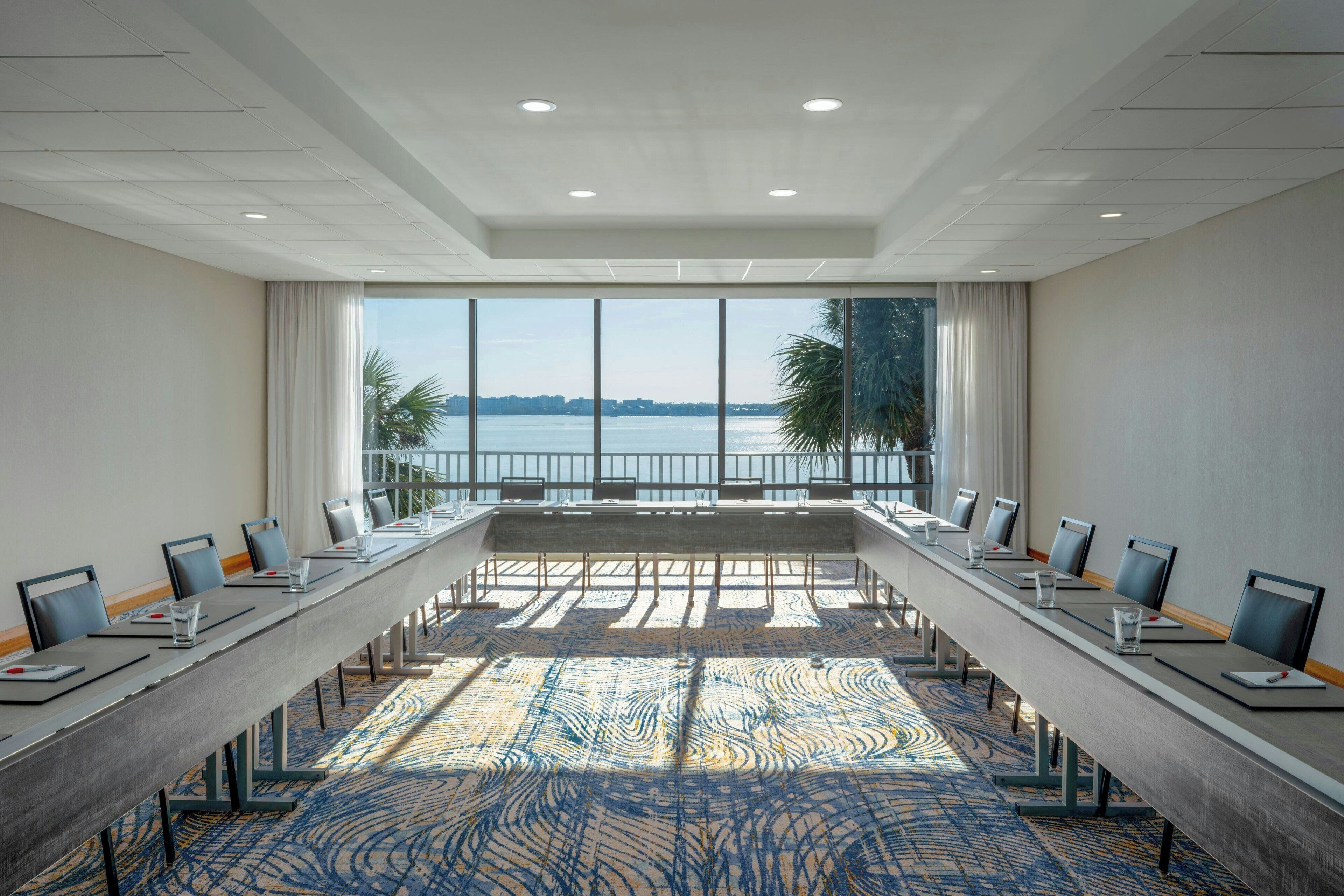 Une salle de conférence avec une longue table, des chaises et une vue sur l’eau et les palmiers.