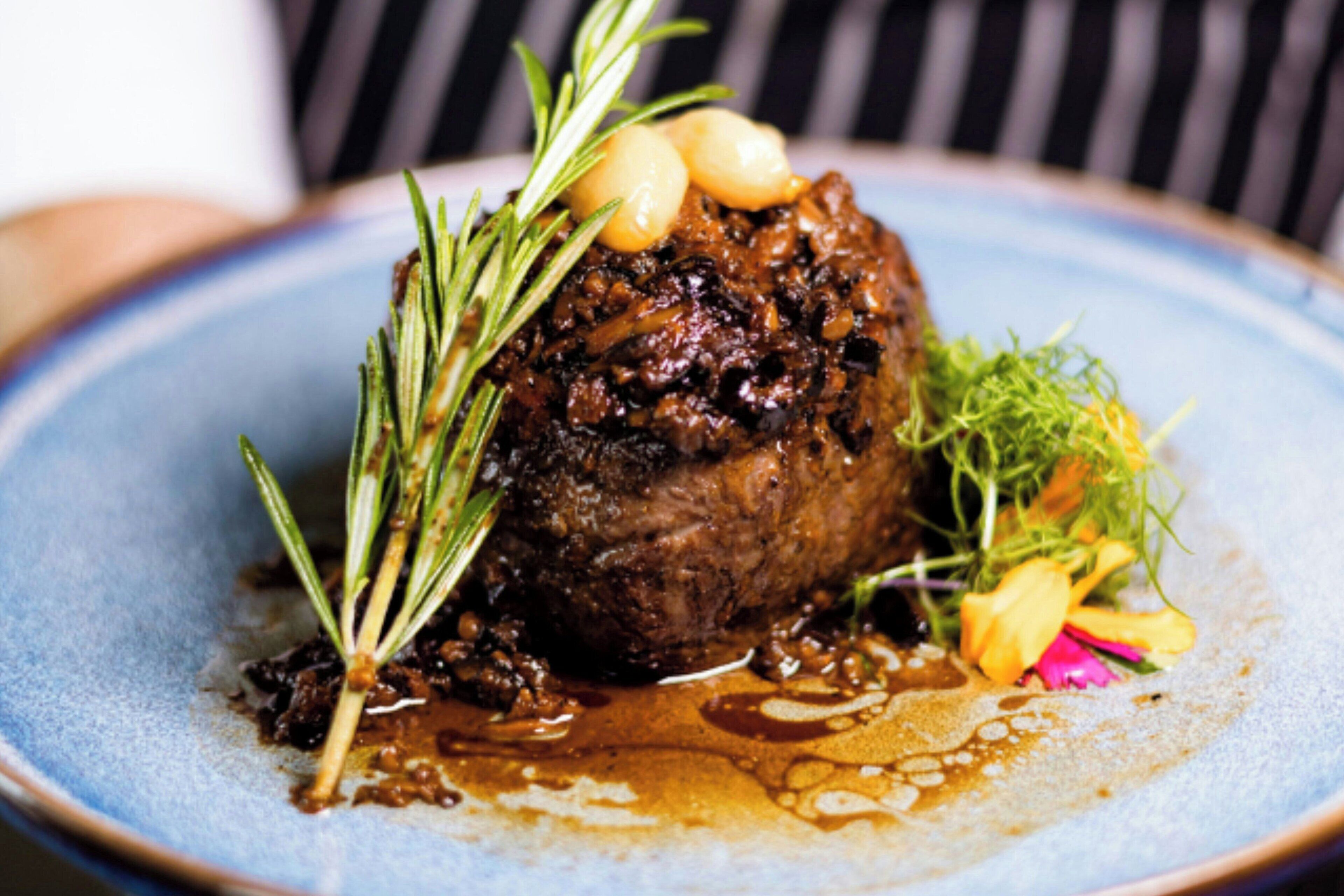 A plated dish with a dark sauce, garnished with rosemary and garlic cloves, served on a blue ceramic plate.