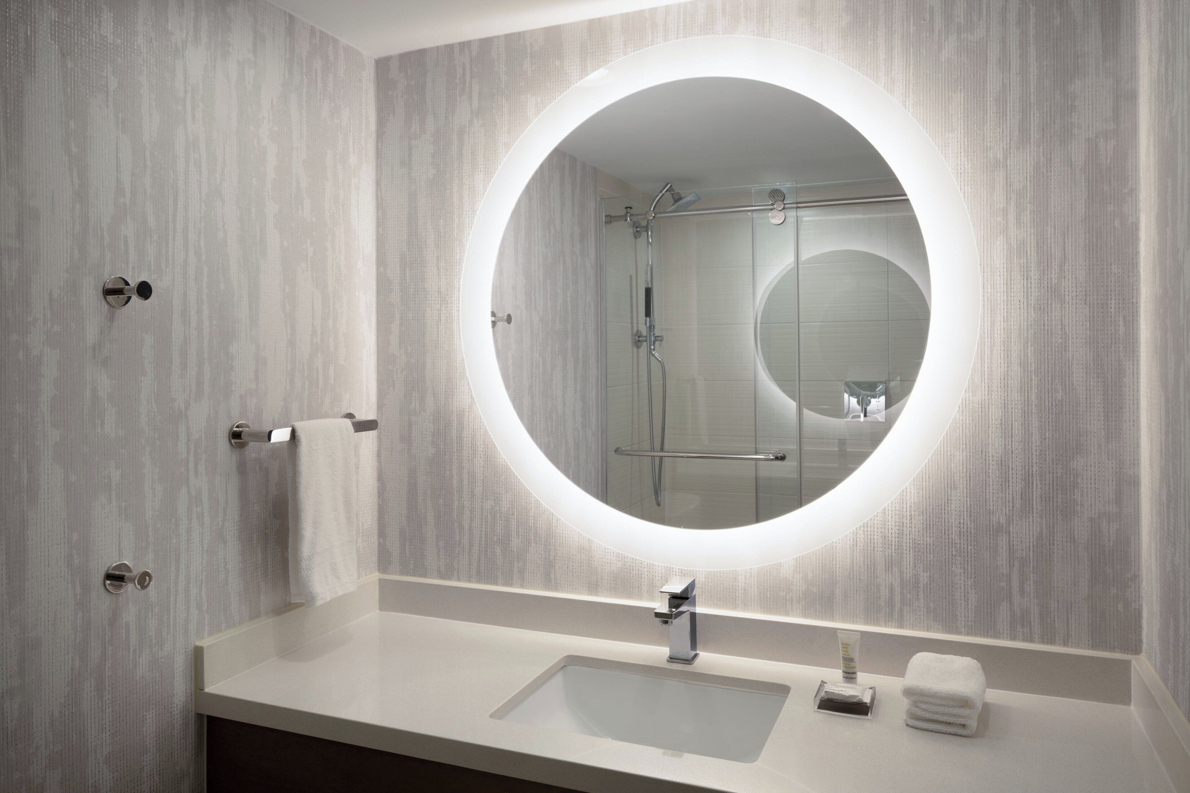 A modern bathroom with a round mirror, a sink, and a shower.