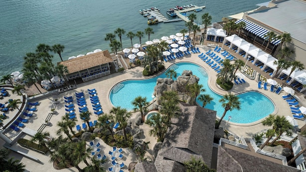 A resort with a large pool surrounded by palm trees and blue lounge chairs. There are multiple boats docked at the pier.