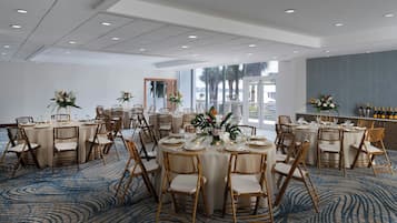 A spacious banquet hall with round tables, wooden chairs, and a blue carpet.
