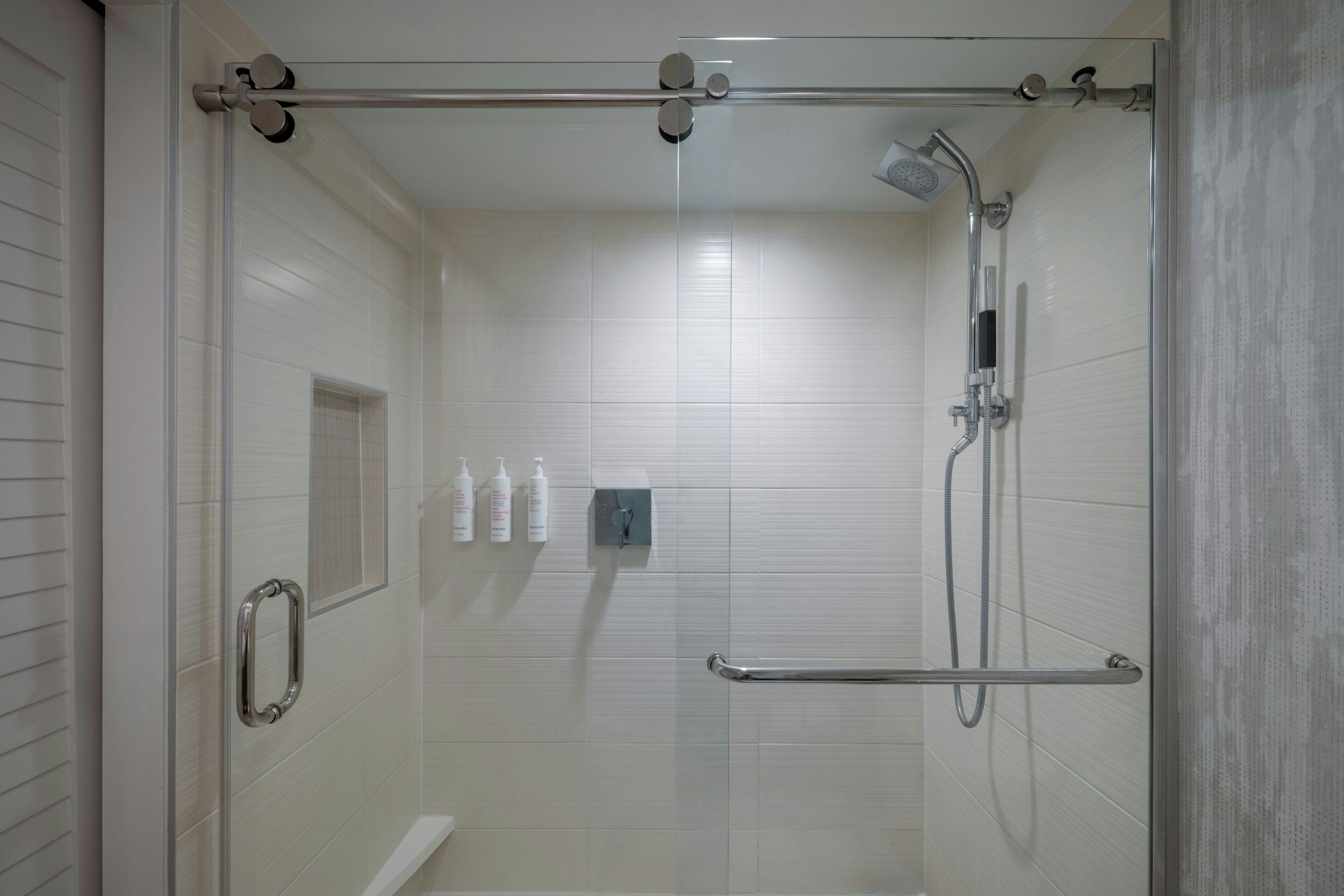 A glass-enclosed shower area with a handheld showerhead, a handheld shower attachment, and a handheld faucet.