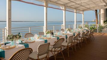 A covered outdoor dining area with tables set for a meal, overlooking a body of water.