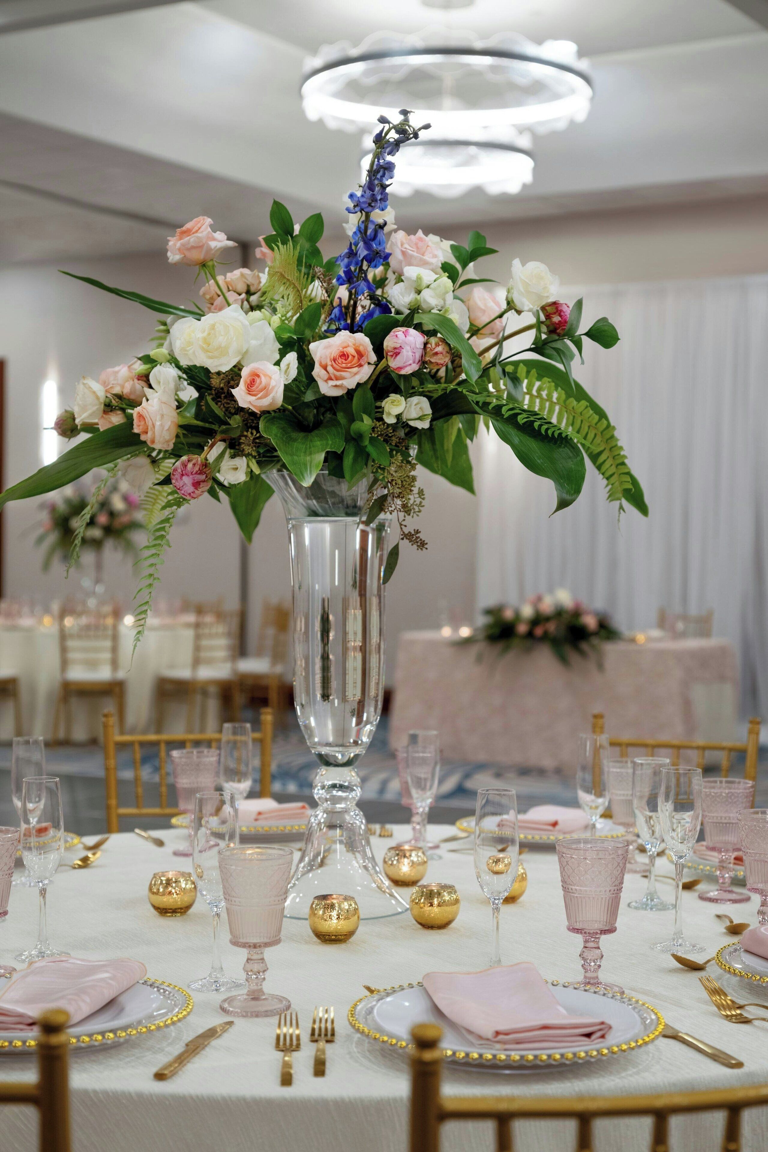 A table set with pink and white flowers, gold accents, and clear glassware.
