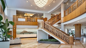 A spacious lobby with a central staircase, a reception desk, and a large decorative light fixture.