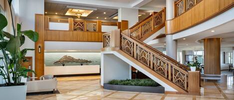 Un amplio vestíbulo con una escalera central, un mostrador de recepción y una gran lámpara decorativa.