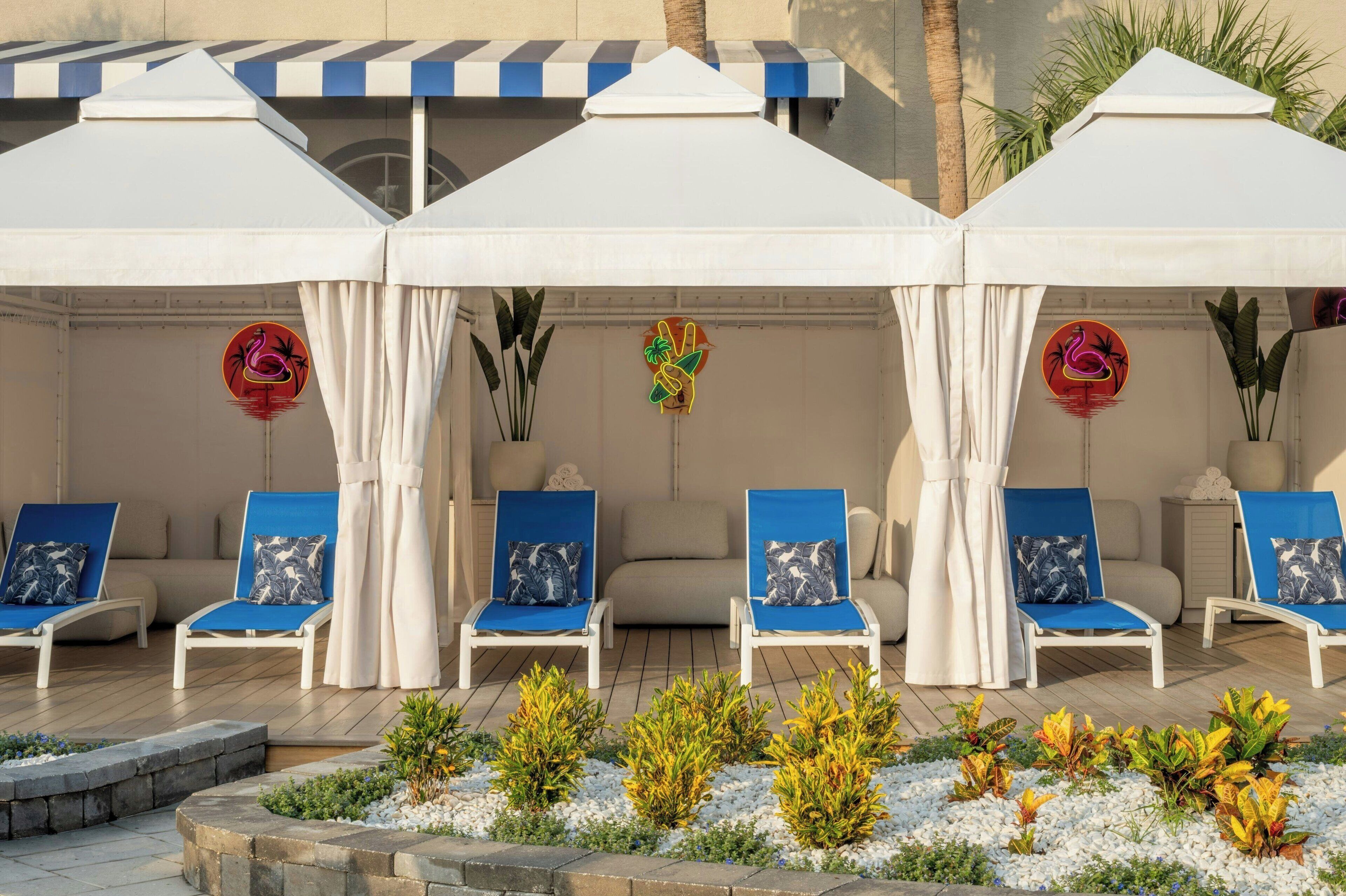 A covered outdoor seating area with white canopies, blue cushioned chairs, and small potted plants.