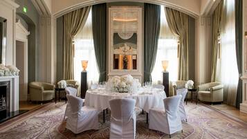 Een stijlvolle eetzaal met een ronde tafel gedekt voor een maaltijd, omringd door witte stoelen, in een ruimte met elegante inrichting en grote ramen.