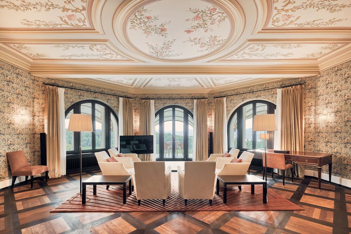 A luxurious room with a large arched window, a flat-screen TV, and a seating area with sofas and chairs.