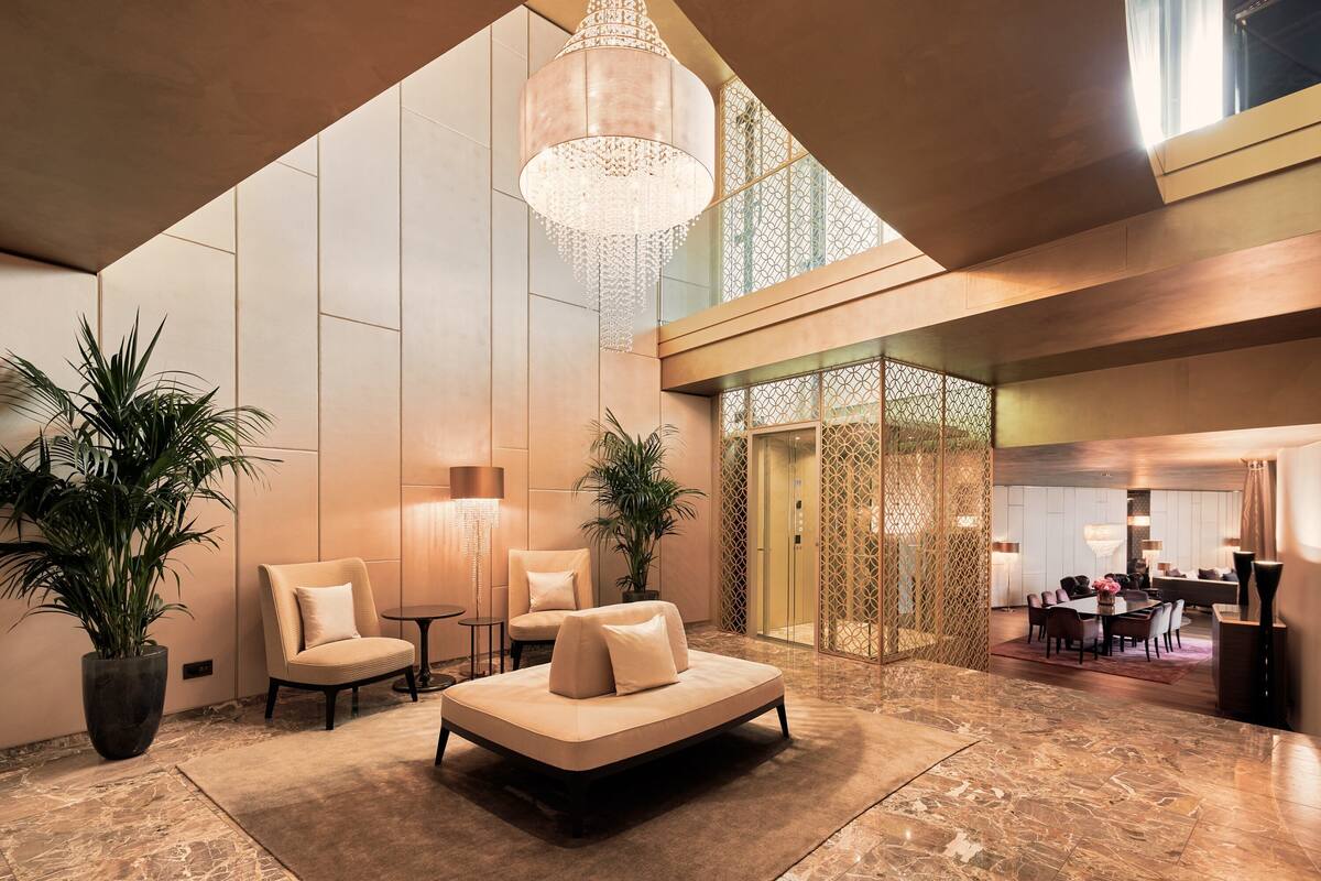 A spacious lobby with a modern design, featuring a large seating area, a chandelier, and potted plants.