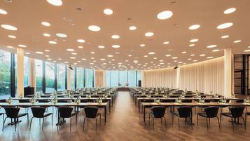 Un salón de conferencias con varias mesas y sillas, ventanas amplias y un techo con luces circulares.