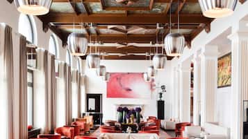 A spacious hotel lobby with red upholstered chairs, a long table, and a large painting on the wall.