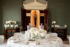 A formal dining table set for a meal with white flowers, candles, and silverware.