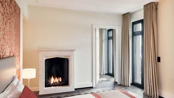 A hotel room with a fireplace, a bed, a nightstand, and a view through a large window.