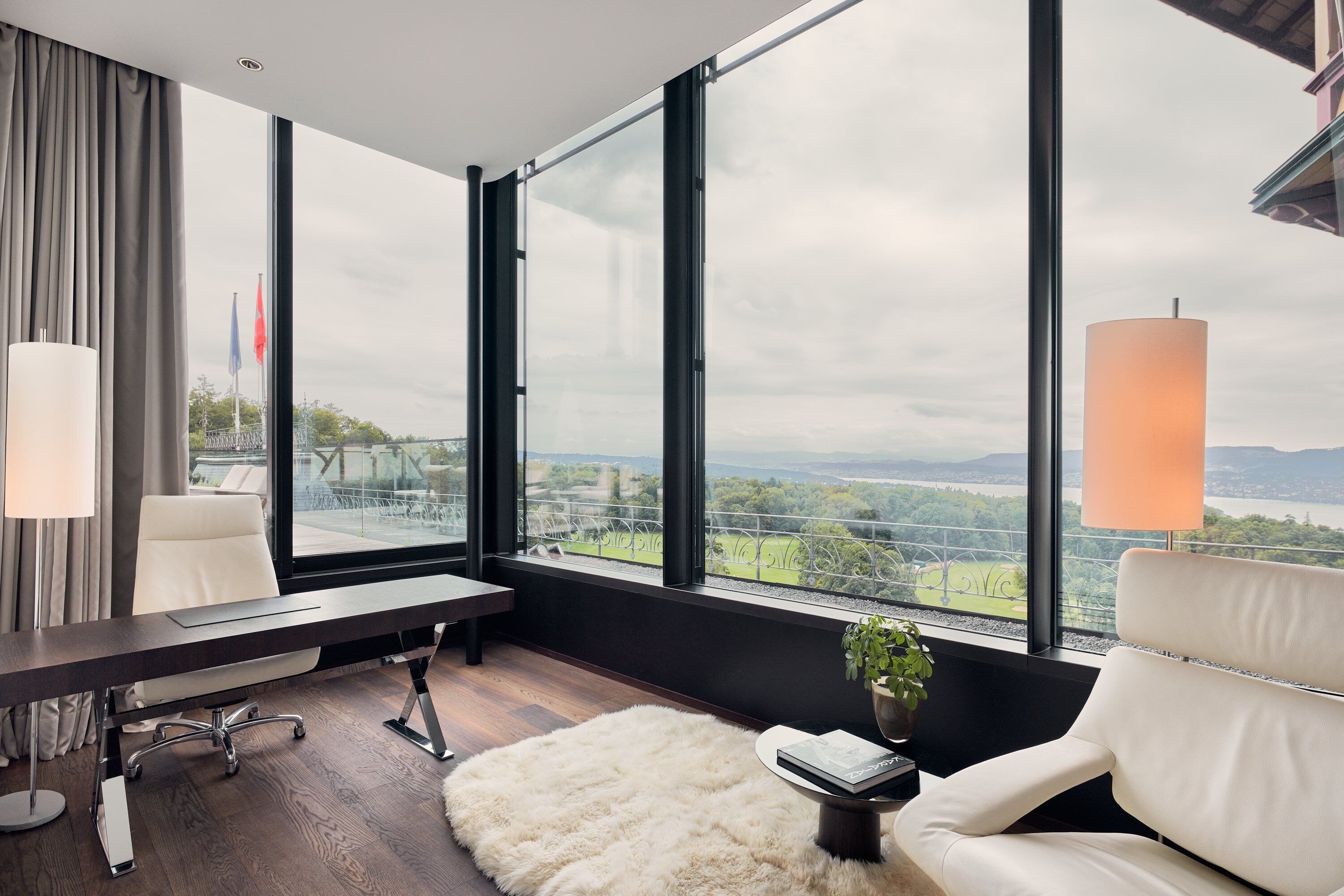 Een moderne hotelkamer met een groot raam, een bureau, een stoel, een lamp en een kamerplant.