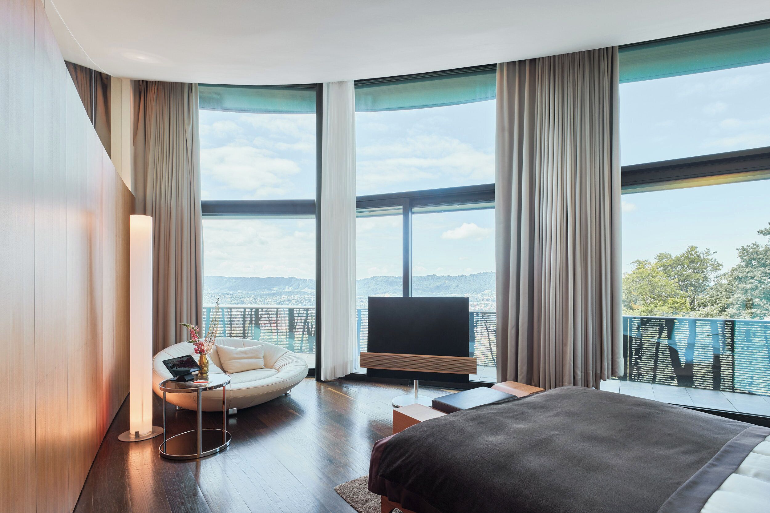 Une chambre d’hôtel moderne dotée d’un grand lit, d’un canapé, d’une télévision et d’un balcon offrant une vue sur la ville.