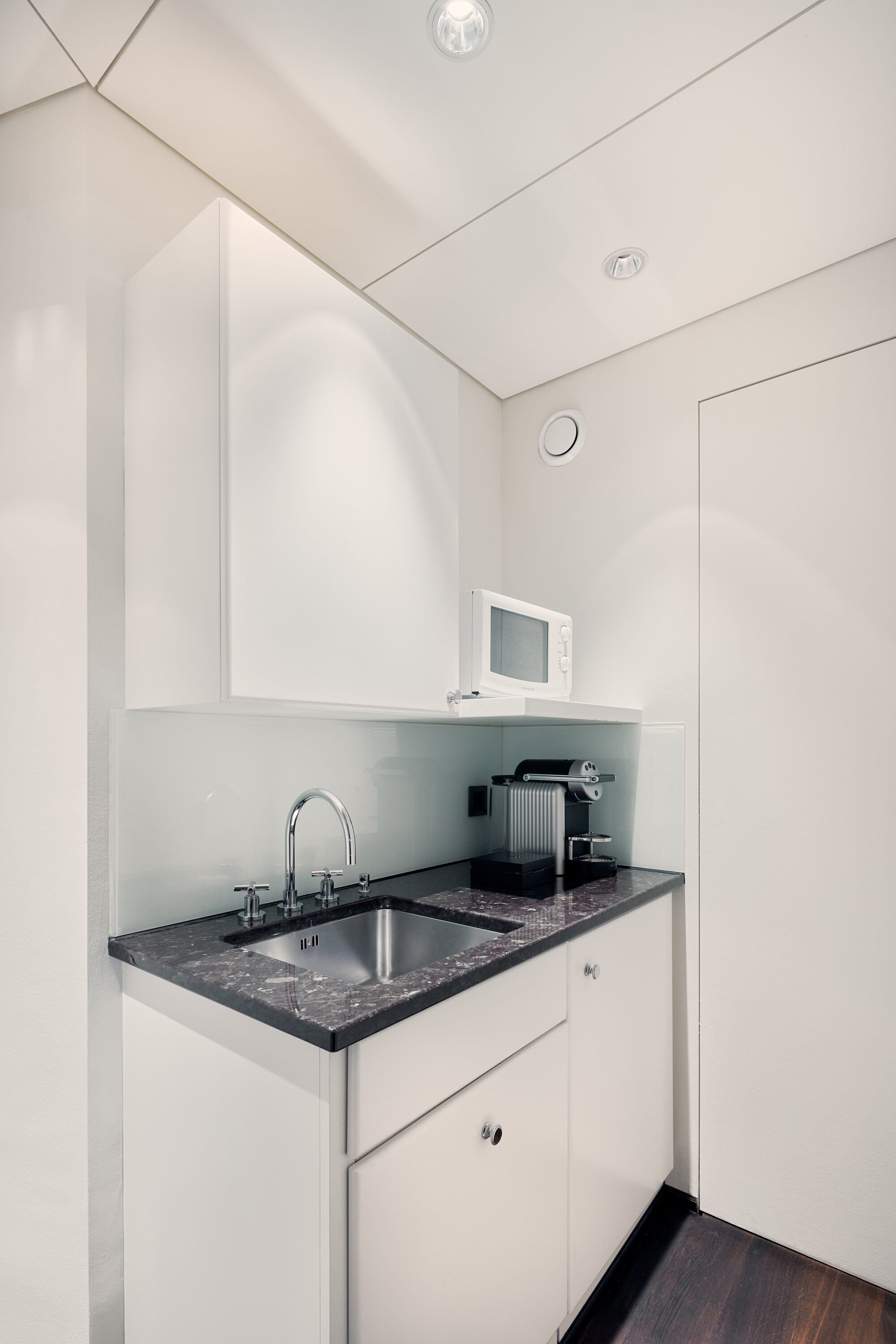 Een kleine keuken met een ingebouwde magnetron, een spoelbak en een koffieapparaat.