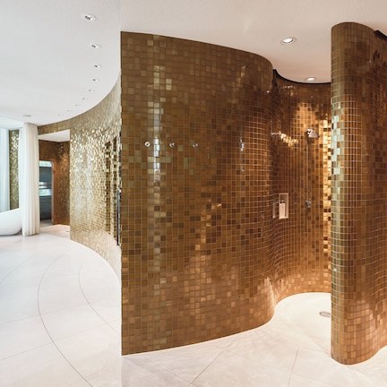 A spacious lobby with a curved wall featuring a mosaic tile design, a white floor, and a large window with natural light.