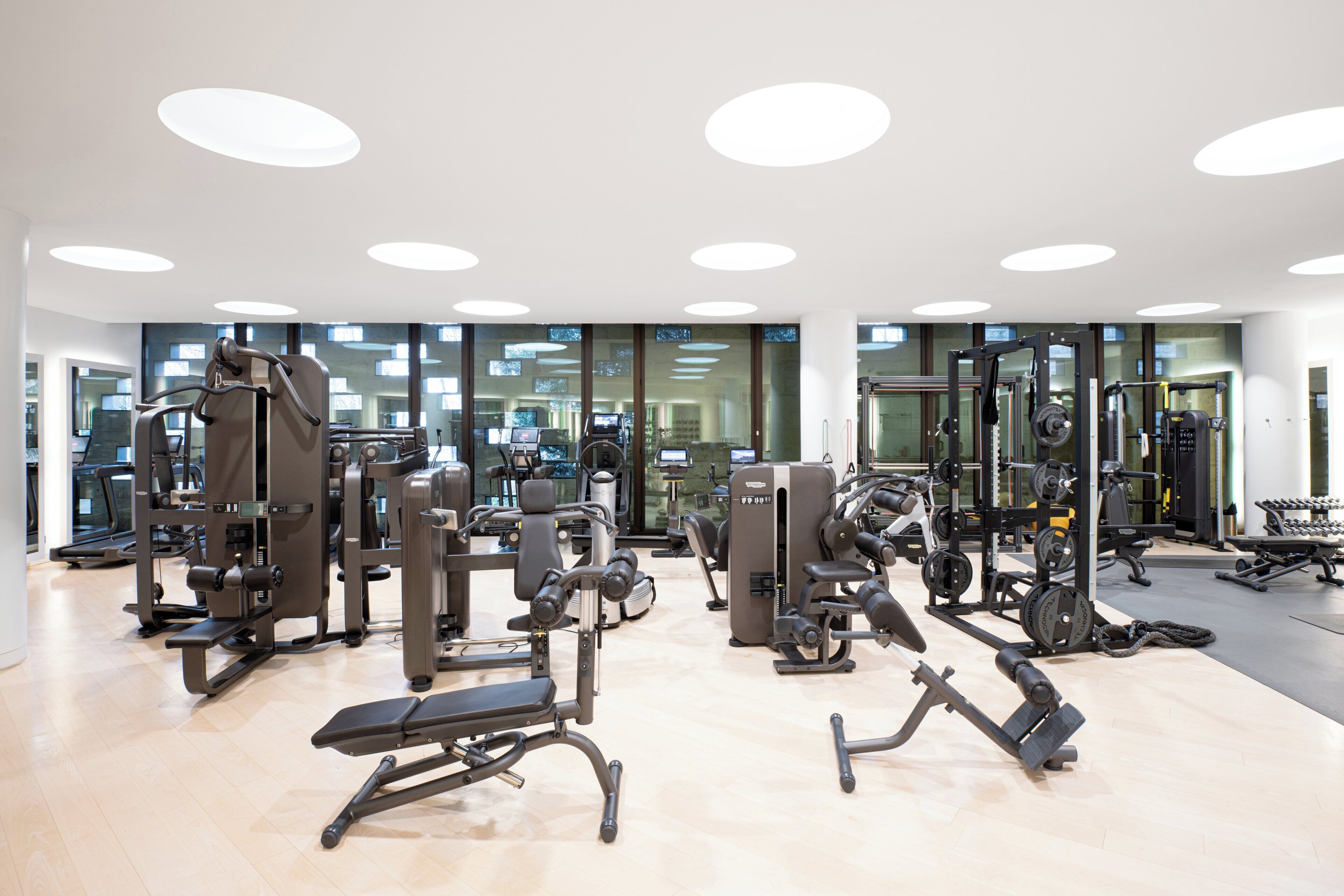 A modern gym with various exercise machines, large windows, and a clean, well-lit interior.