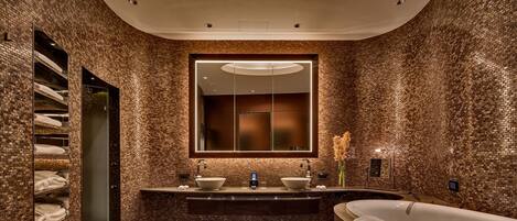 Un baño moderno con pared de ladrillo, un espejo grande, lavabo doble y bañera independiente.
