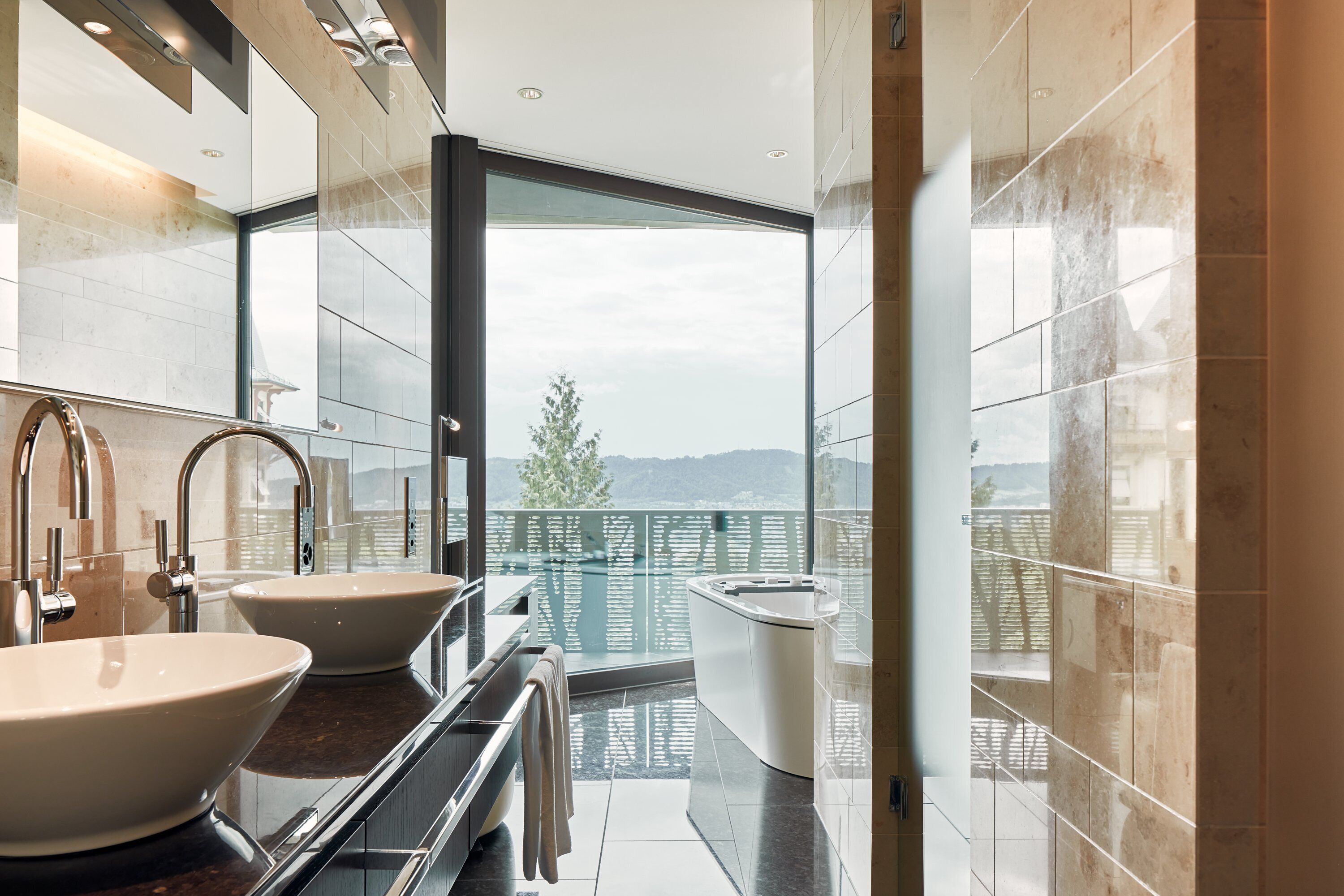 Une salle de bain moderne avec deux lavabos, une baignoire et une grande fenêtre donnant sur un balcon.