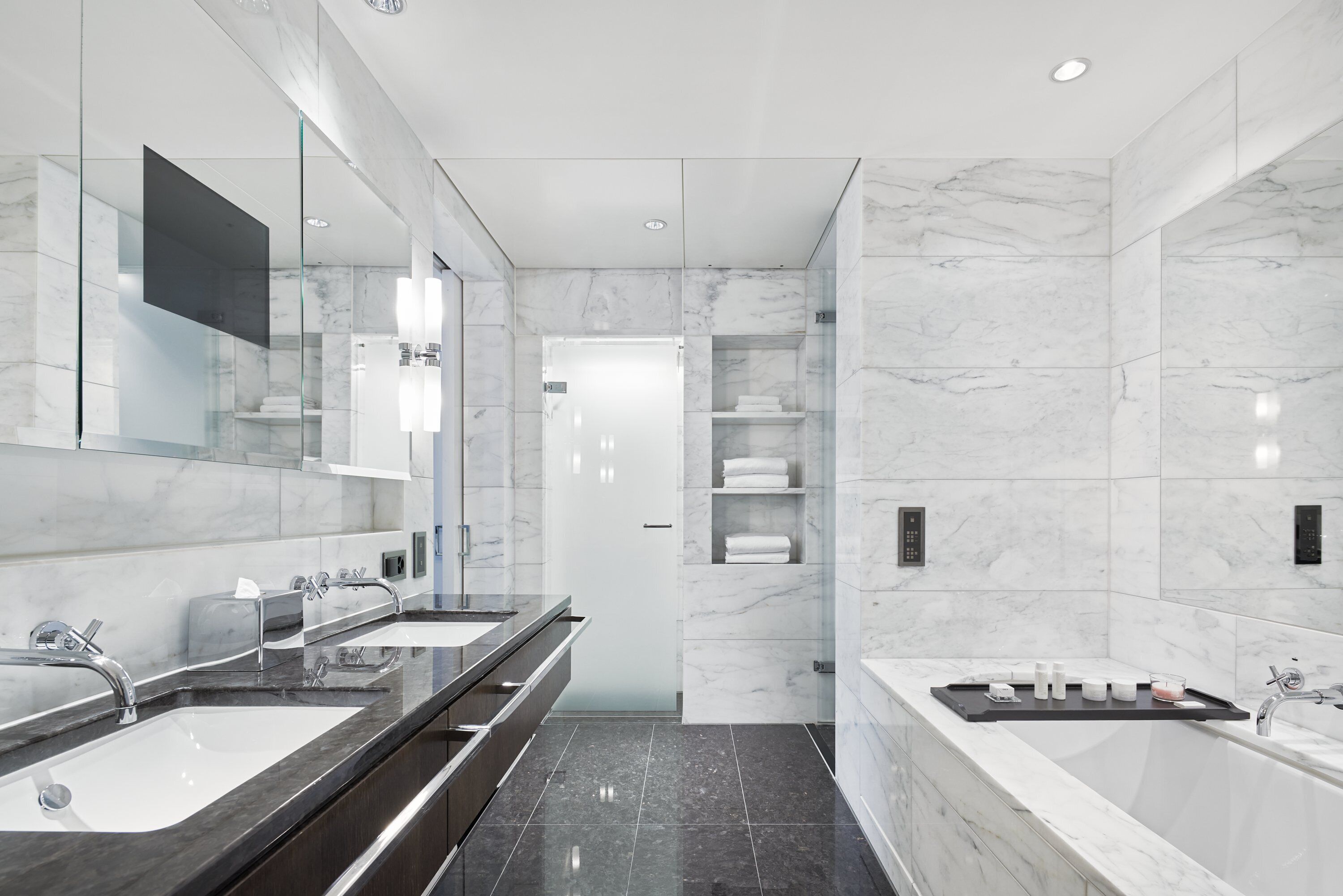 A modern bathroom with two sinks, a large mirror, and a bathtub.