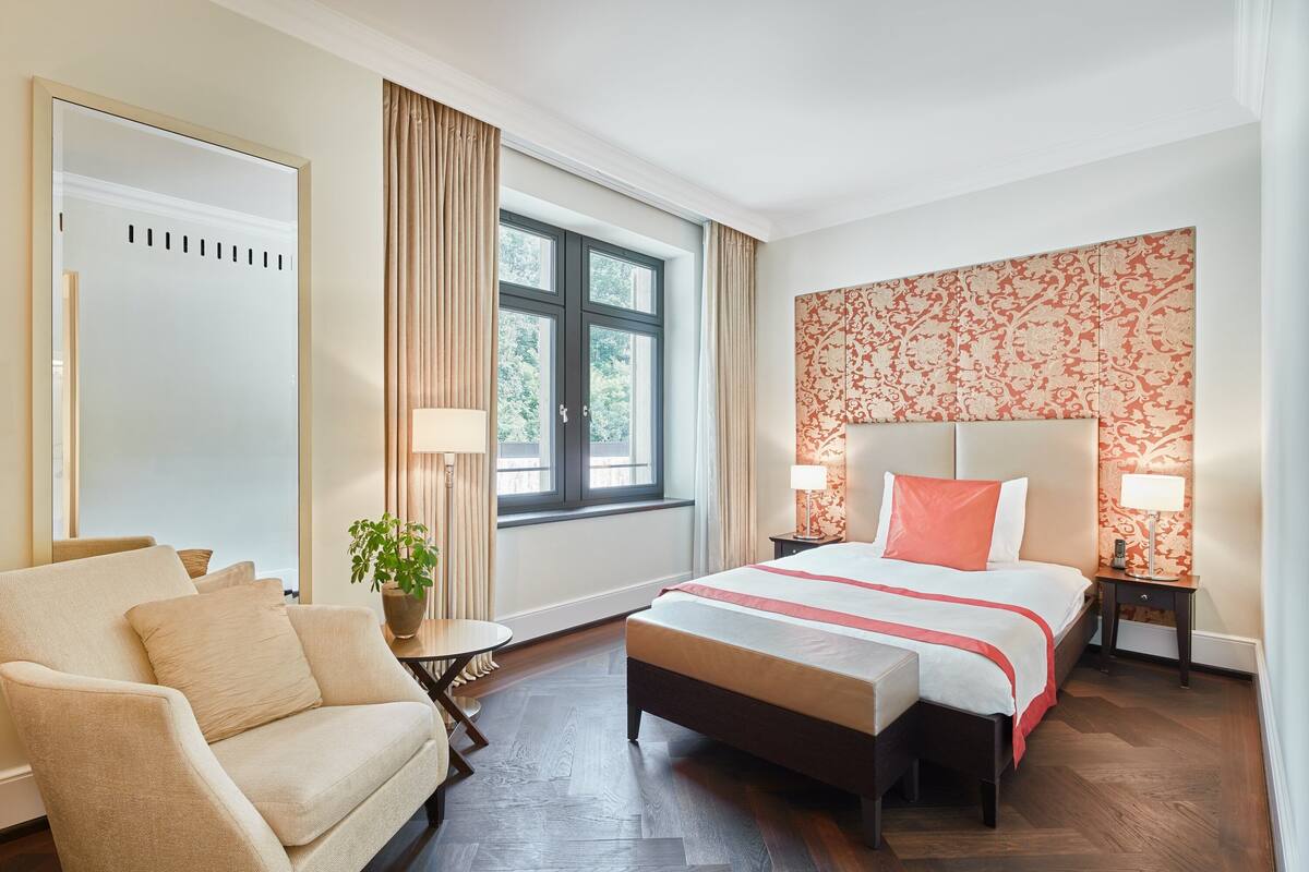 A hotel room with a bed, a sofa, a small table, a potted plant, and a window with curtains.