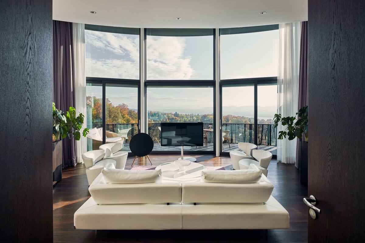 A modern living room with a large curved window, a flat-screen TV, and a white sectional sofa.