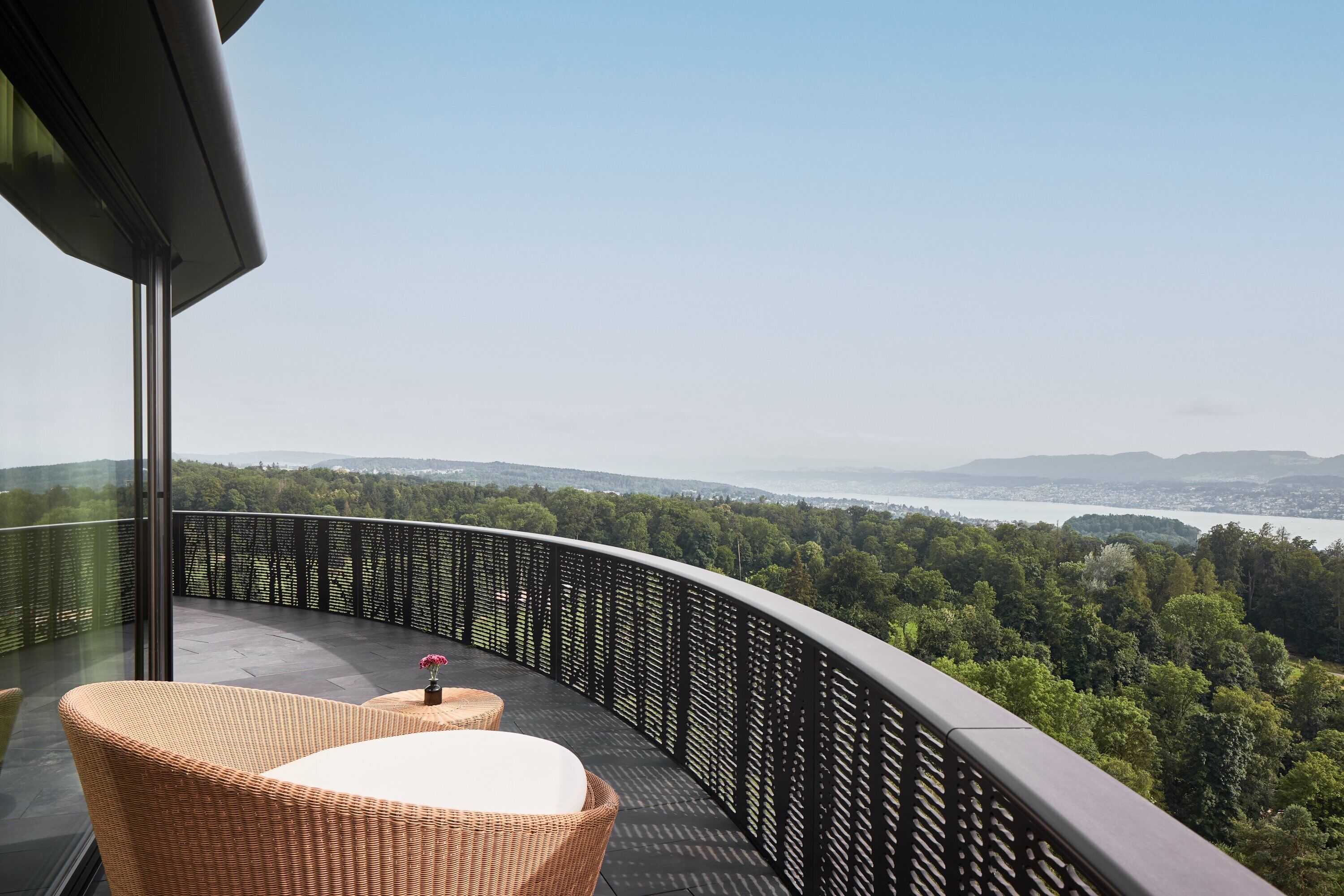 Ein Balkon mit Korbmöbeln und Blick auf Wald und Wasser.