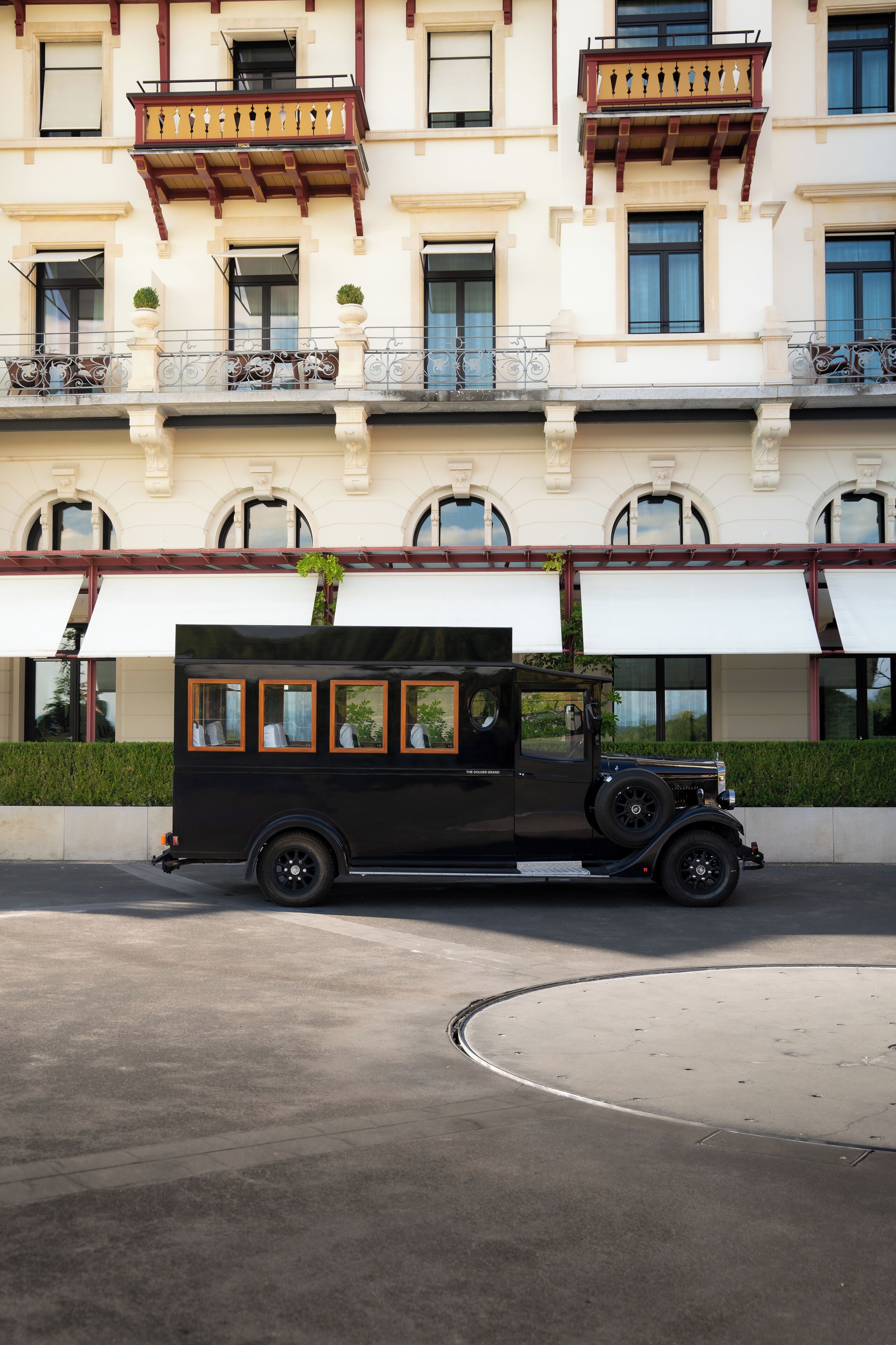 A vintage black car parked in front of a building with balconies and large windows.
