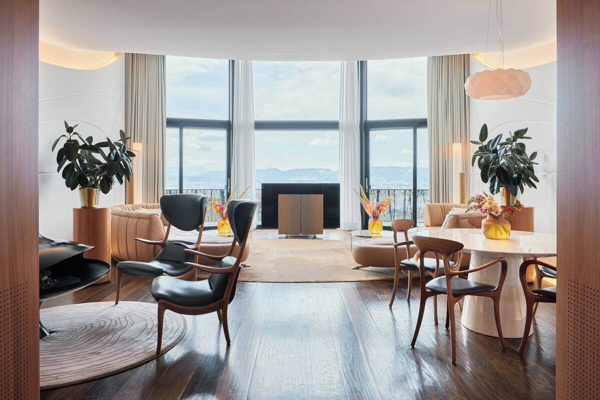 A modern living room with a large window, a fireplace, and a dining area with a round table and chairs.