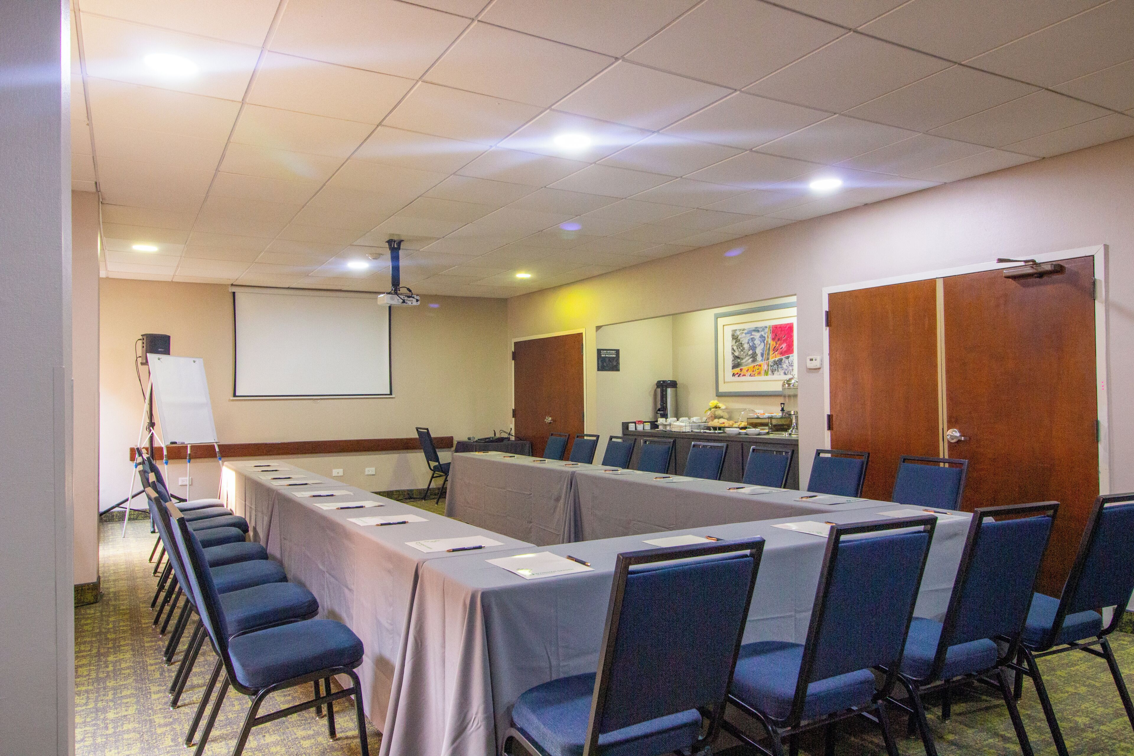 Un salón de conferencias con una larga mesa, sillas, un proyector y una pantalla.