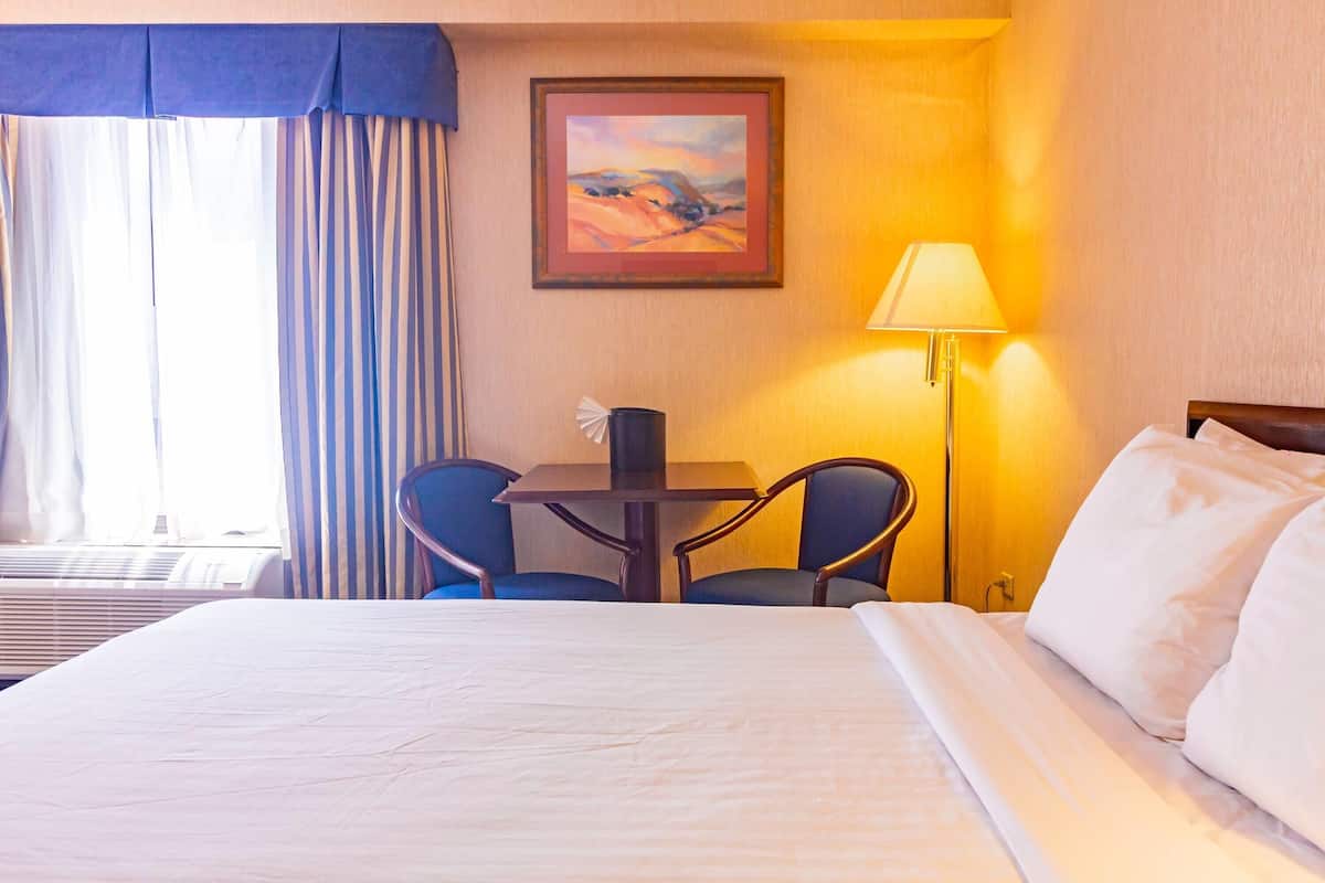 Habitación de hotel con cama, una mesa y dos sillas, una lámpara y un cuadro en la pared.