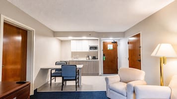 Una habitación de hotel con kitchenette, zona de comedor con mesa y sillas, sofá, escritorio y lámpara.