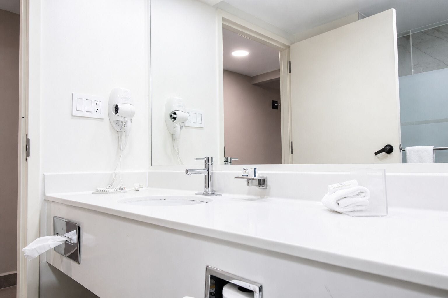 A modern bathroom with a large mirror, two hair dryers, a sink, and a towel rack.
