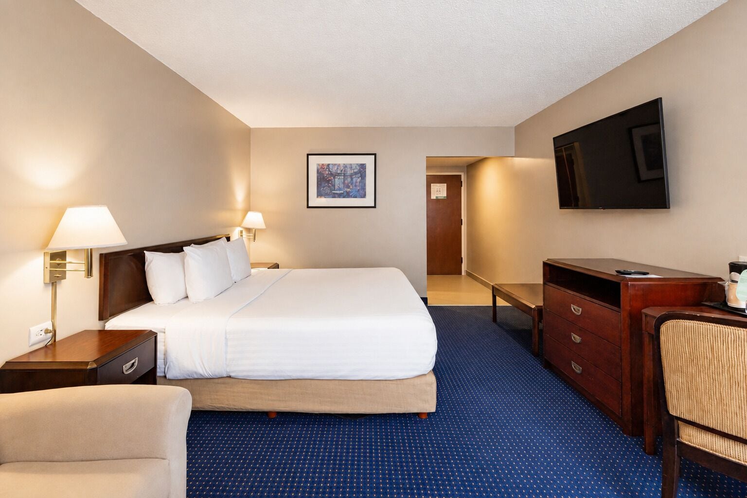 Habitación de hotel con cama, escritorio, silla, televisión e imagen en la pared.