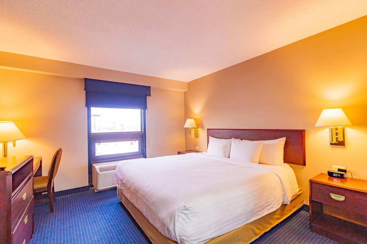 Una habitación de hotel con una cama, lámparas de noche, un escritorio y una silla.