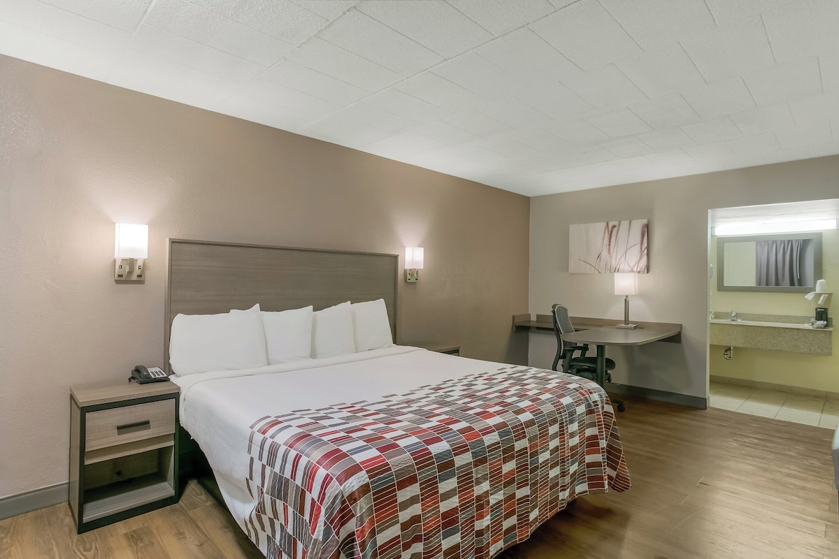 Habitación de hotel con cama, mesita de noche, lámpara, escritorio, silla y baño con espejo.