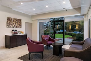 A modern hotel lobby with a reception desk, seating area, and large glass doors leading to a garden view. - Red Roof Inn Baltimore (Baltimore)