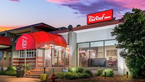 Um Red Roof Inn com toldo vermelho, uma escadaria que leva à entrada e uma área externa bem cuidada com vegetação.