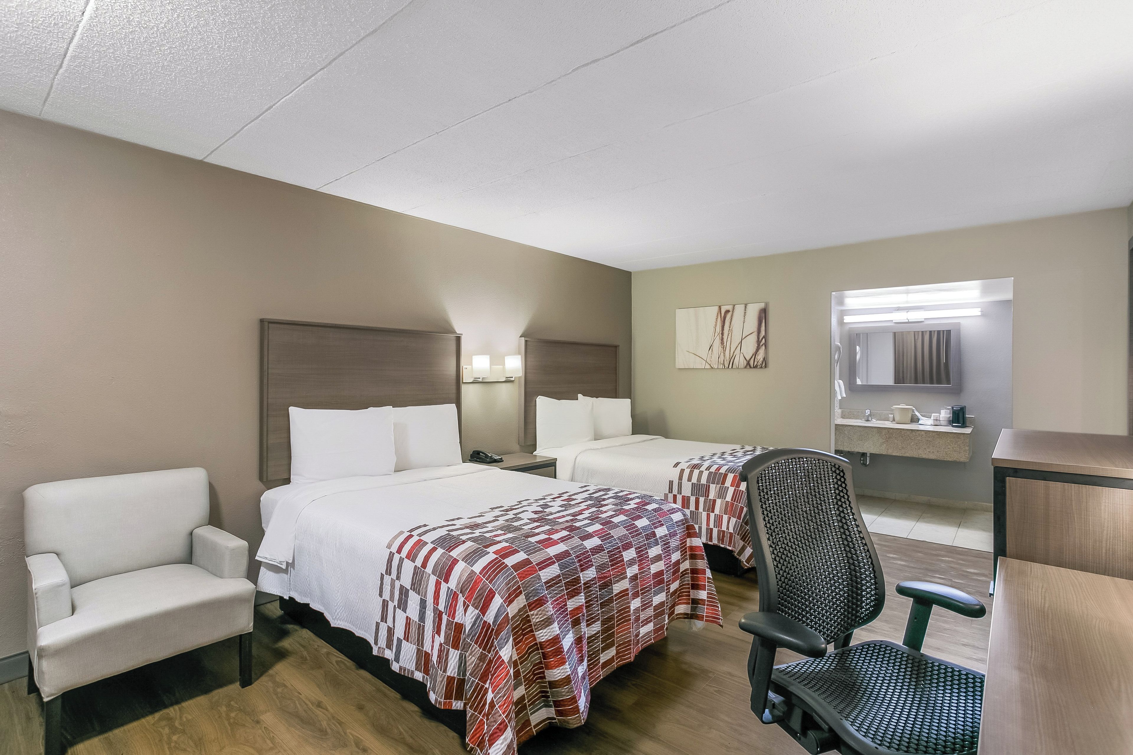 A hotel room with two beds, a desk, a chair, and a bathroom.