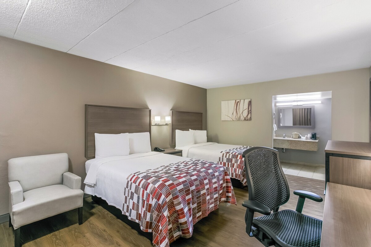 A hotel room with two beds, a desk, a chair, and a bathroom.
