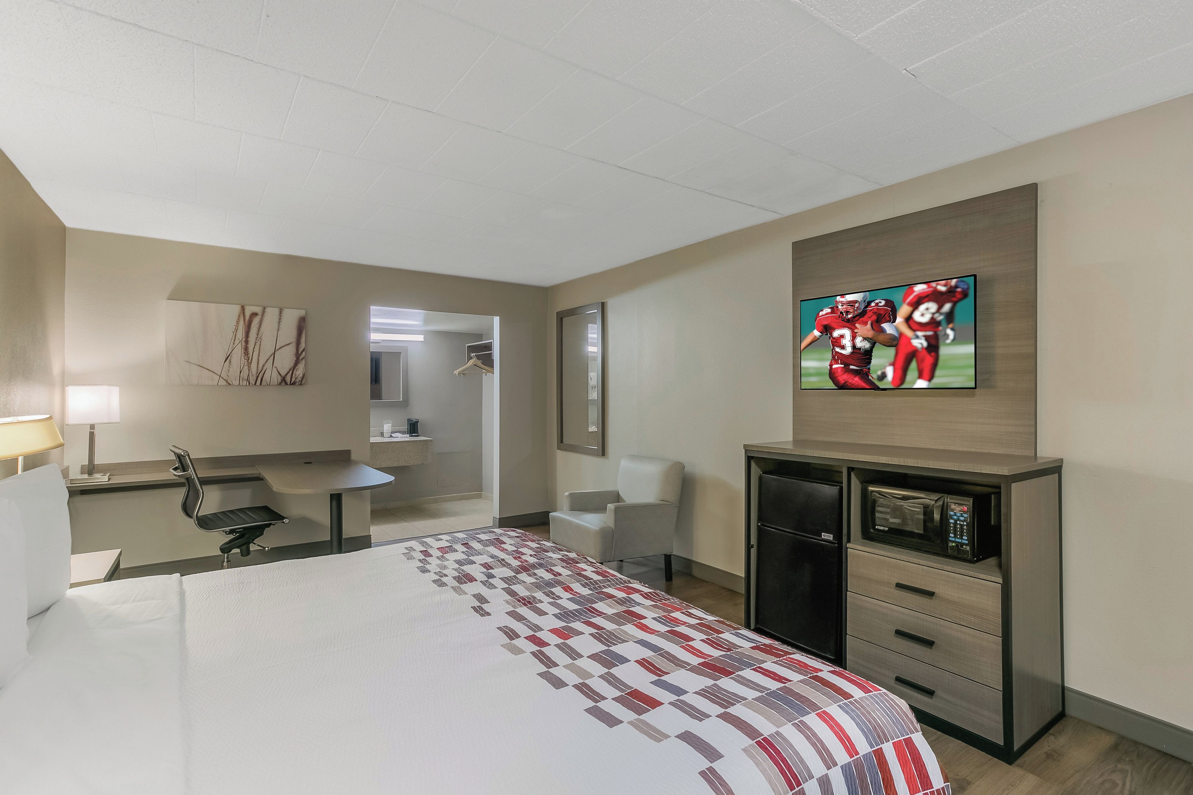 Habitación de hotel con cama, escritorio, silla, televisor y microondas.