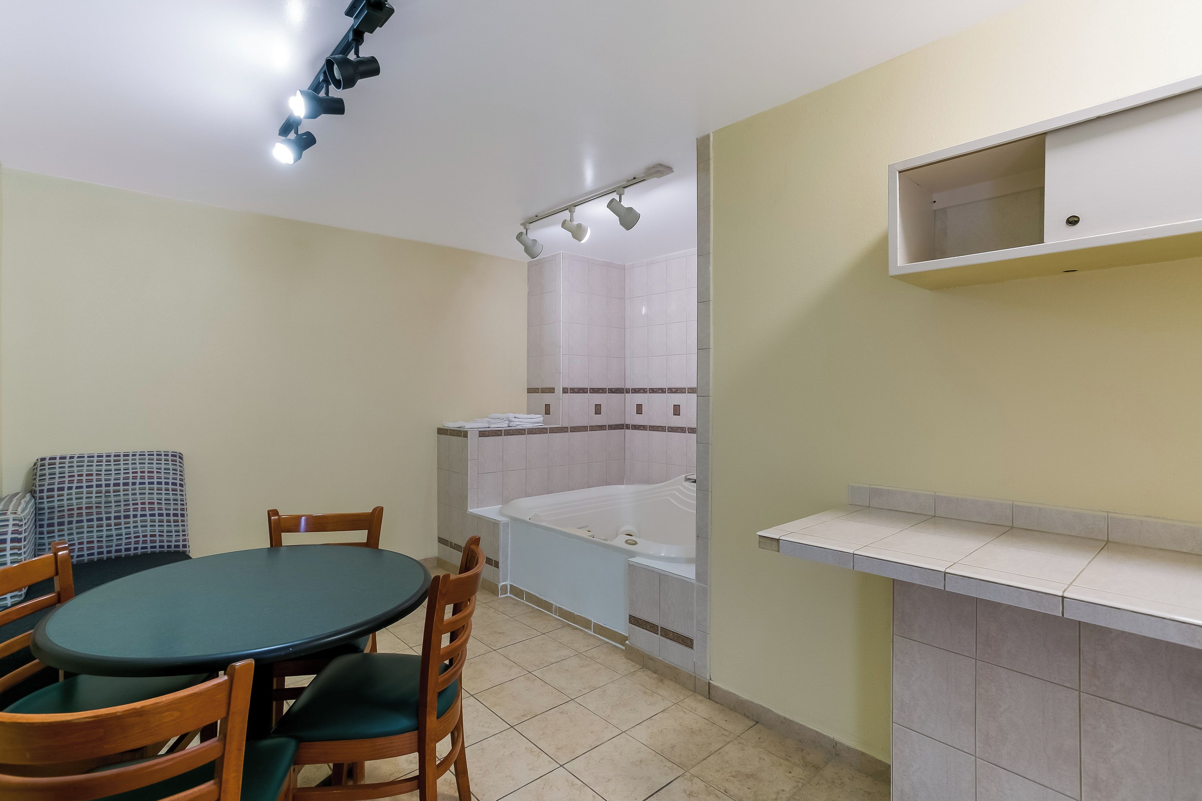 A room with a round table, chairs, a bathtub, and a small shelf.