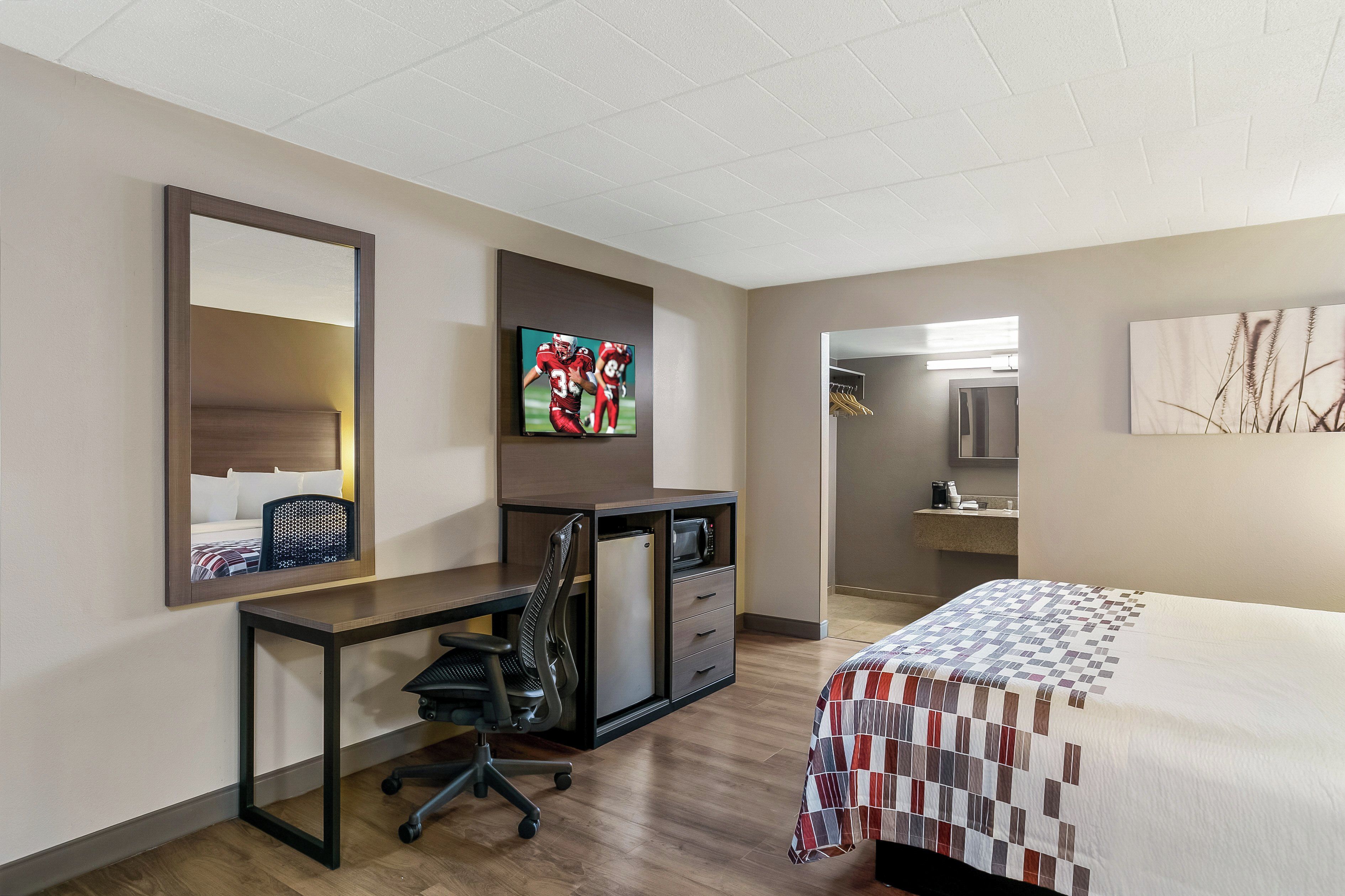 A hotel room with a bed, a desk with a chair, a television, and a bathroom.